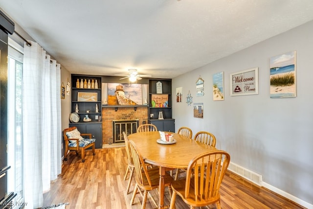 dining area with ceiling fan, hardwood / wood-style flooring, a brick fireplace, and a textured ceiling