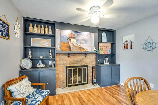 living room with ceiling fan, a textured ceiling, a brick fireplace, and light hardwood / wood-style floors