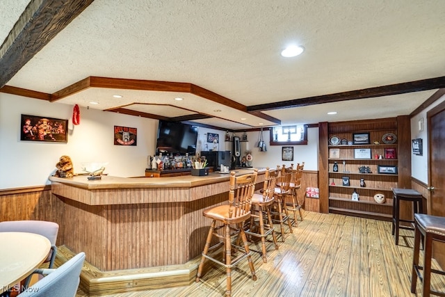 bar featuring wood walls, hardwood / wood-style floors, beam ceiling, and a textured ceiling