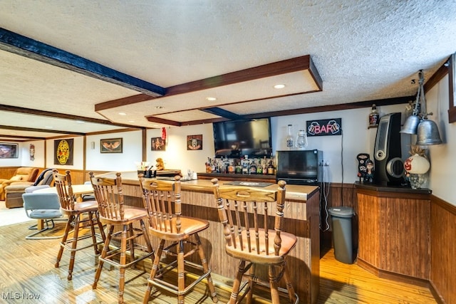 bar featuring light hardwood / wood-style floors, beamed ceiling, and a textured ceiling