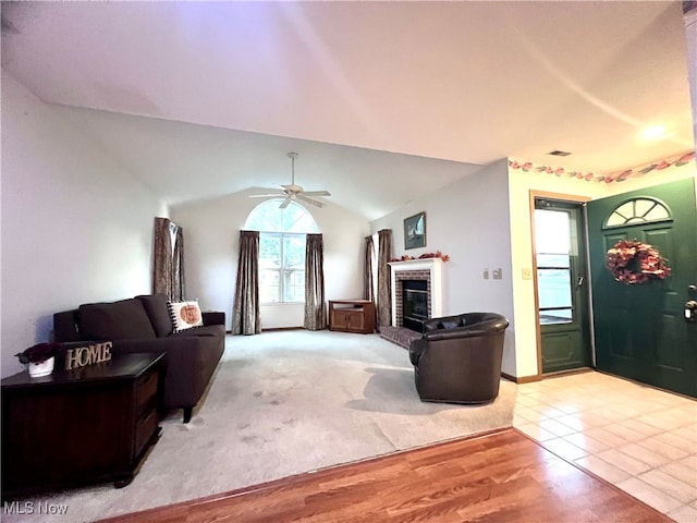 living room with ceiling fan, light hardwood / wood-style floors, lofted ceiling, and a brick fireplace