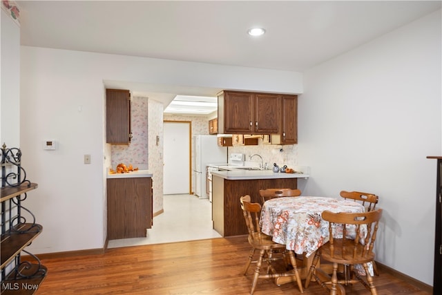 kitchen featuring kitchen peninsula, white appliances, light hardwood / wood-style flooring, and sink