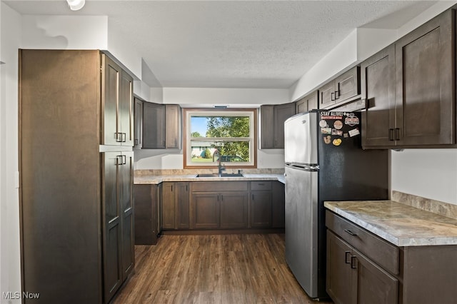 kitchen with dark hardwood / wood-style floors, sink, dark brown cabinetry, a textured ceiling, and stainless steel refrigerator