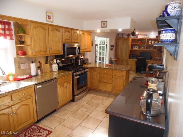 kitchen with light tile patterned flooring, stainless steel appliances, kitchen peninsula, and dark stone counters