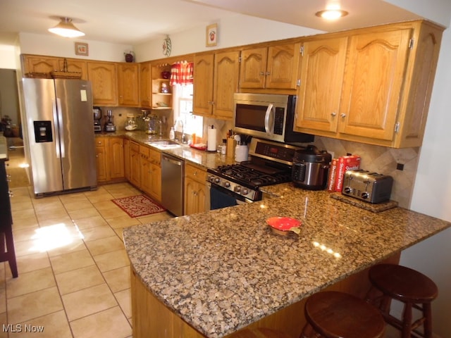 kitchen with light stone counters, stainless steel appliances, sink, kitchen peninsula, and backsplash