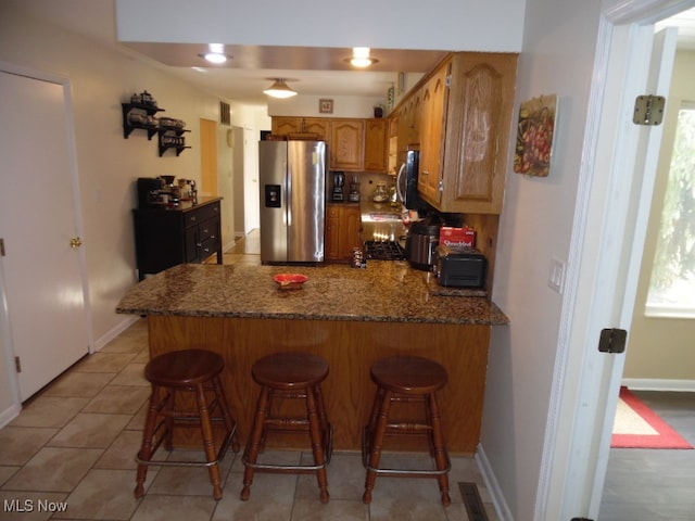 kitchen featuring stainless steel appliances, kitchen peninsula, dark stone countertops, and a kitchen breakfast bar