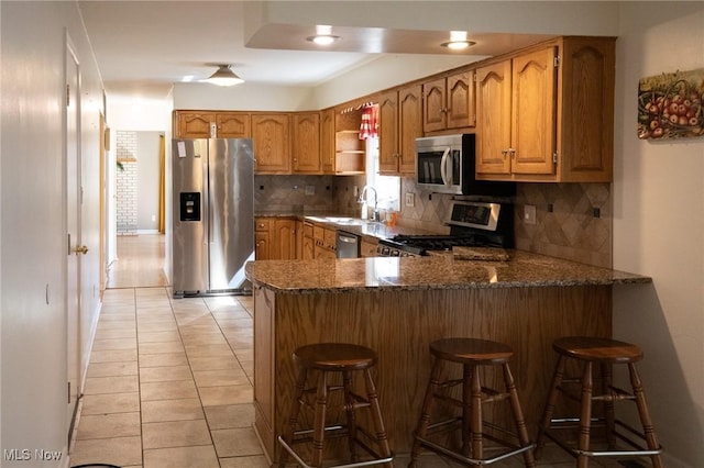 kitchen with dark stone countertops, a peninsula, a sink, decorative backsplash, and stainless steel appliances