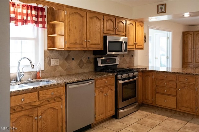 kitchen with backsplash, dark stone countertops, brown cabinetry, stainless steel appliances, and a sink