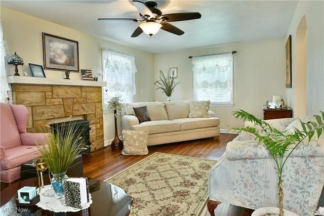 living room featuring dark wood-type flooring, ceiling fan, a fireplace, and a healthy amount of sunlight