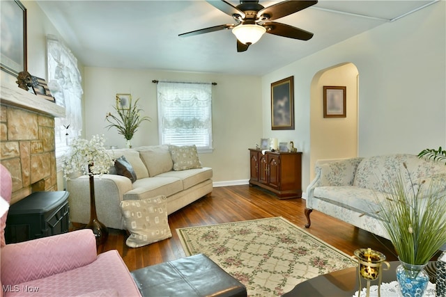 living room featuring ceiling fan, a stone fireplace, and dark hardwood / wood-style floors