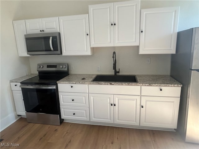 kitchen featuring stainless steel appliances, light hardwood / wood-style flooring, white cabinets, and sink