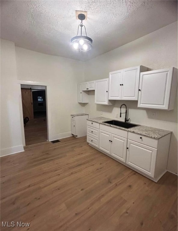 kitchen with dark hardwood / wood-style floors, white cabinets, sink, pendant lighting, and a barn door