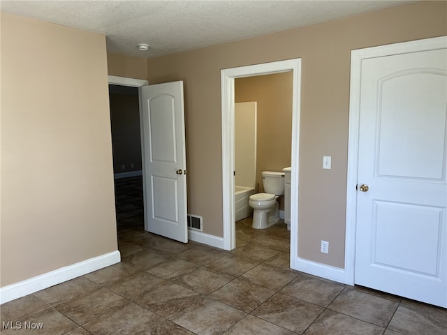 unfurnished bedroom with tile patterned floors, a textured ceiling, and ensuite bathroom