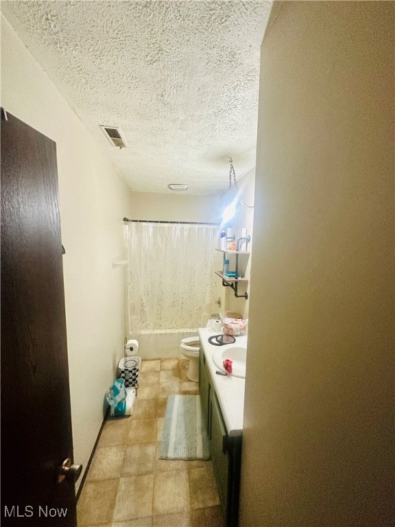 full bathroom featuring a textured ceiling, shower / bath combo, vanity, and toilet