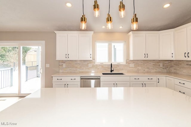 kitchen featuring white cabinetry, backsplash, decorative light fixtures, stainless steel dishwasher, and sink