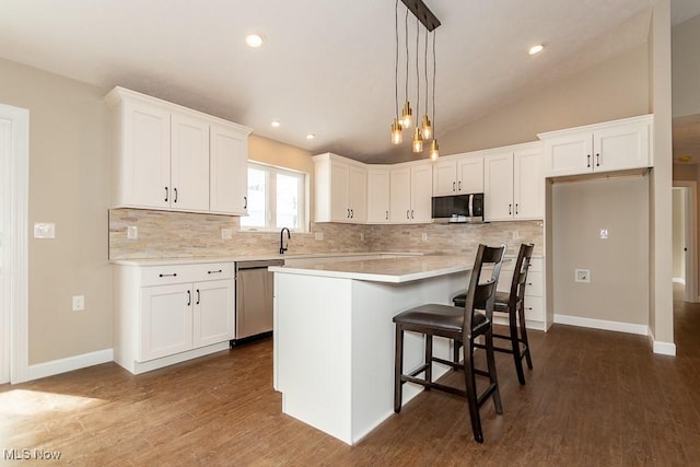 kitchen with decorative light fixtures, lofted ceiling, a kitchen island, stainless steel appliances, and white cabinets