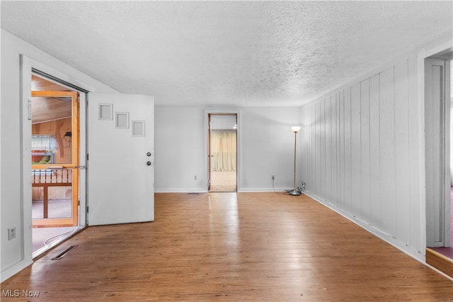 spare room with light hardwood / wood-style flooring, a textured ceiling, and wooden walls