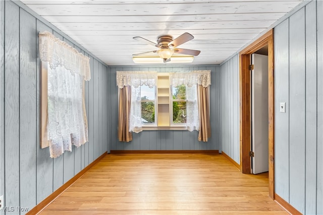 empty room with wood walls, wood ceiling, light hardwood / wood-style floors, and ceiling fan