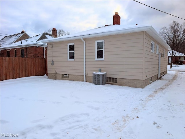 snow covered rear of property featuring central AC unit