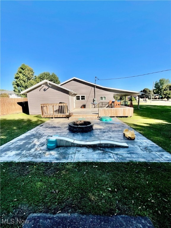 back of house with an outdoor fire pit, a wooden deck, and a lawn