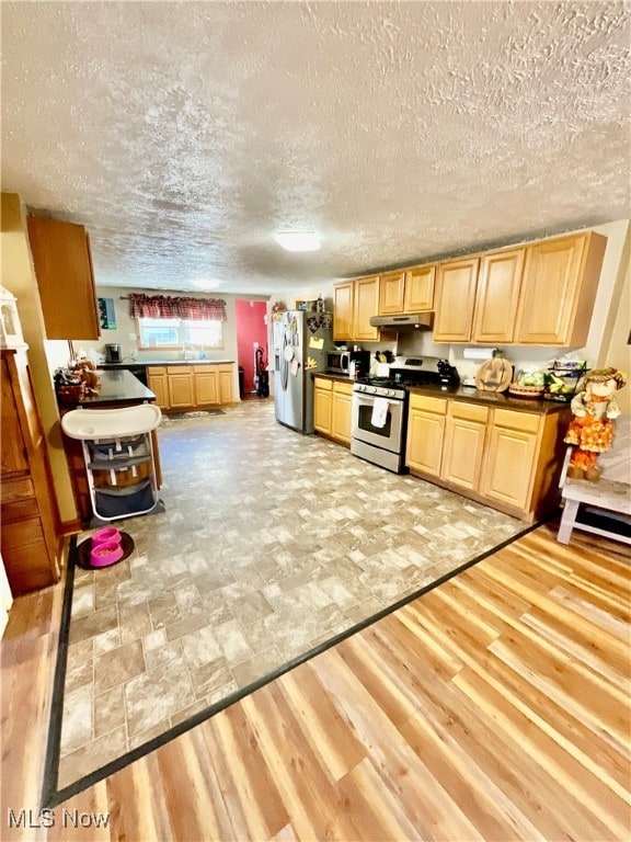 kitchen with stainless steel appliances, light brown cabinetry, light wood-type flooring, and a textured ceiling