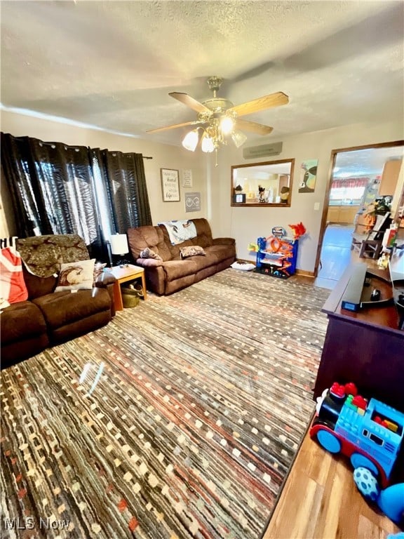 living room featuring wood-type flooring, a wall unit AC, a textured ceiling, and ceiling fan