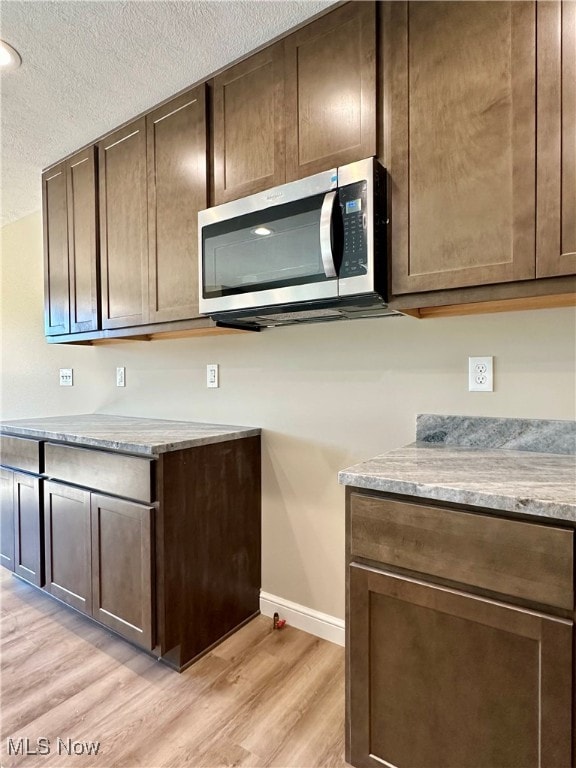 kitchen with dark brown cabinets, light stone countertops, a textured ceiling, and light hardwood / wood-style flooring