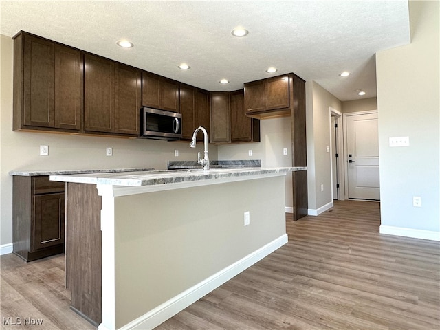 kitchen with dark brown cabinetry, a center island with sink, and light wood-type flooring