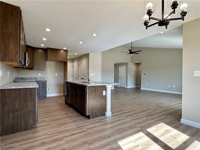 kitchen with lofted ceiling, sink, a textured ceiling, a center island with sink, and light wood-type flooring