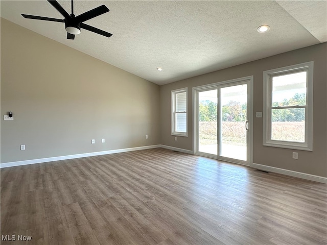 spare room with lofted ceiling, ceiling fan, light hardwood / wood-style flooring, and a textured ceiling