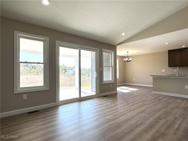 doorway with an inviting chandelier, vaulted ceiling, light hardwood / wood-style flooring, and a textured ceiling