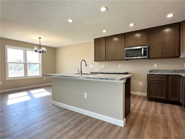 kitchen featuring light hardwood / wood-style floors, a center island with sink, a notable chandelier, sink, and hanging light fixtures