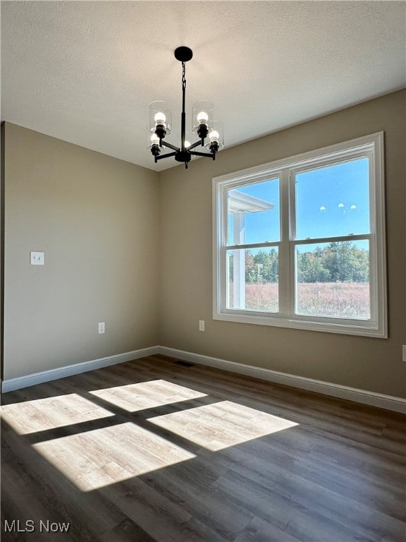 empty room featuring dark hardwood / wood-style floors, a chandelier, and a textured ceiling