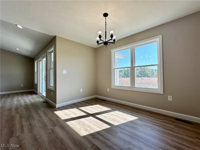 unfurnished dining area featuring vaulted ceiling, a textured ceiling, dark wood-type flooring, and a chandelier