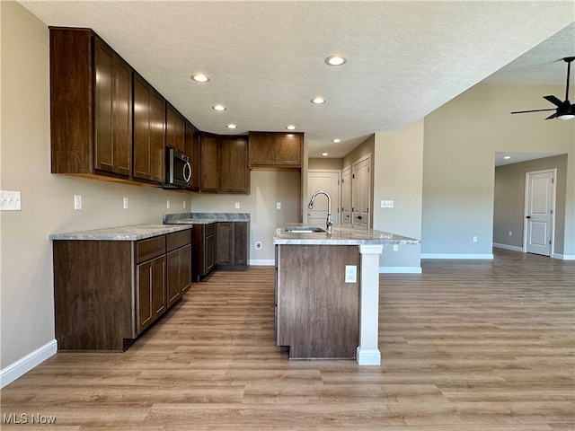 kitchen featuring an island with sink, light wood-type flooring, sink, and a textured ceiling