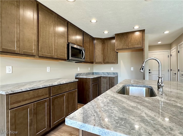 kitchen featuring light hardwood / wood-style floors, a kitchen island with sink, sink, light stone counters, and a textured ceiling