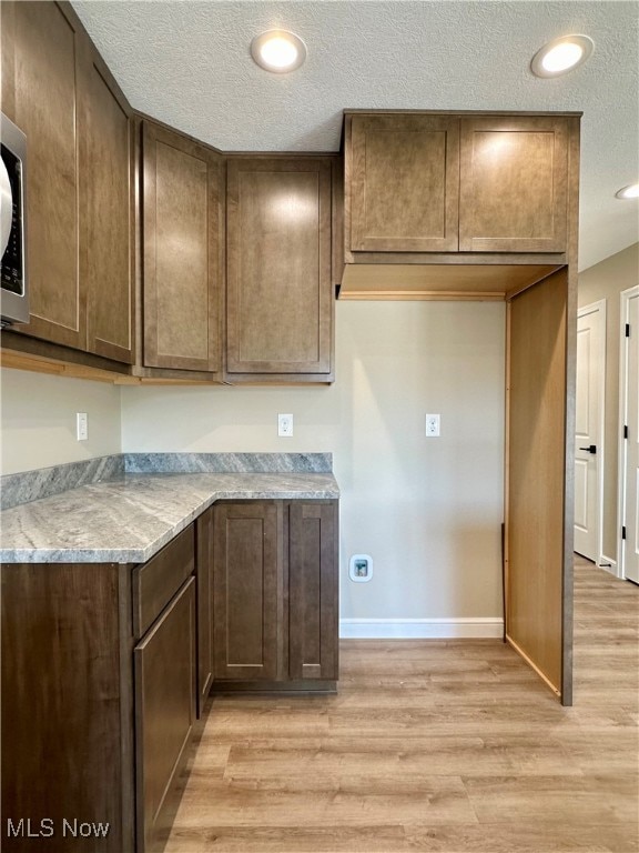 kitchen with a textured ceiling, dark brown cabinets, light stone countertops, and light hardwood / wood-style flooring