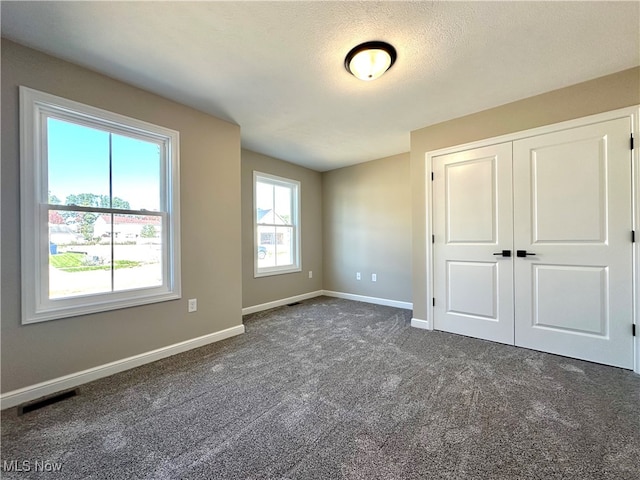 unfurnished bedroom with dark colored carpet, multiple windows, a closet, and a textured ceiling