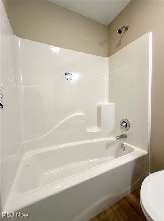 bathroom with hardwood / wood-style flooring, tub / shower combination, and toilet