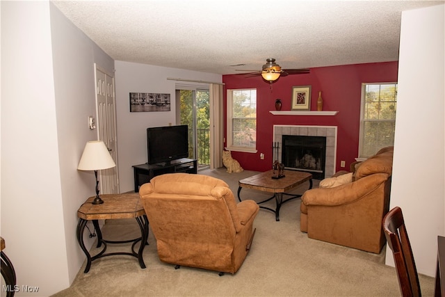 carpeted living room with ceiling fan, a textured ceiling, and a tiled fireplace