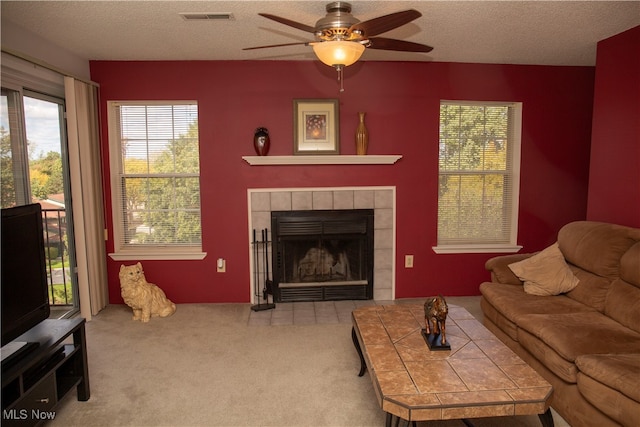 carpeted living room featuring ceiling fan, a textured ceiling, and a tile fireplace