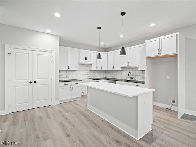 kitchen with hanging light fixtures, sink, backsplash, white cabinetry, and light hardwood / wood-style floors