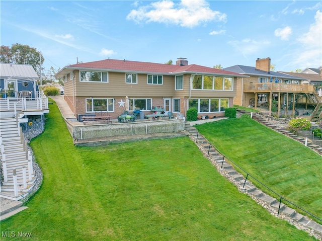 rear view of house featuring a deck, a yard, and a sunroom