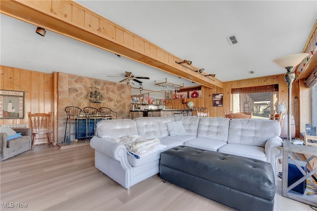 living room featuring ceiling fan, wood walls, a stone fireplace, and light hardwood / wood-style floors