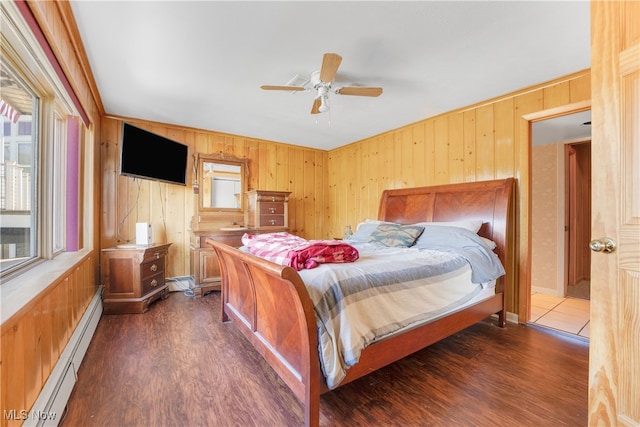 bedroom with dark wood-type flooring, a baseboard heating unit, wooden walls, and ceiling fan