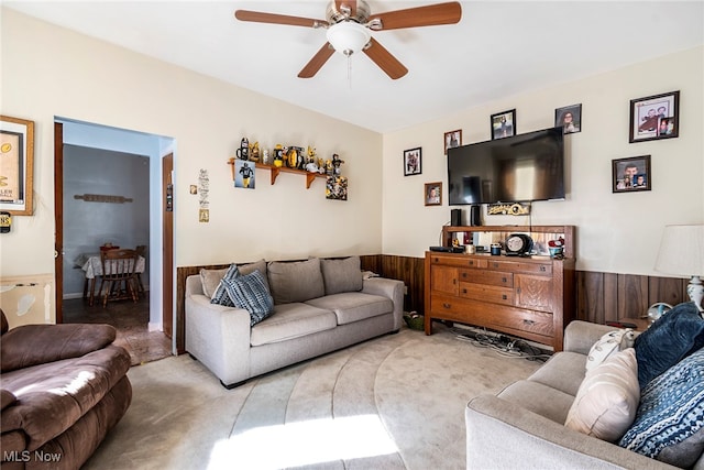 carpeted living room with wooden walls and ceiling fan