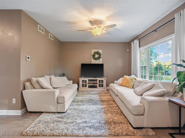 living room with light hardwood / wood-style floors, a textured ceiling, and ceiling fan