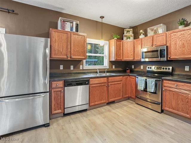 kitchen featuring pendant lighting, sink, a textured ceiling, light hardwood / wood-style flooring, and appliances with stainless steel finishes