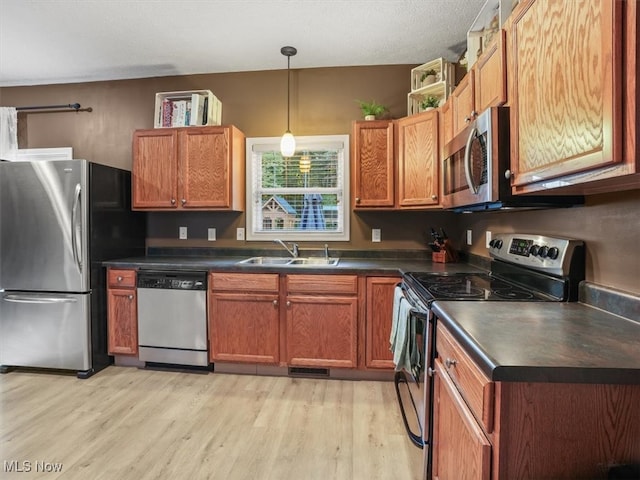 kitchen with appliances with stainless steel finishes, hanging light fixtures, sink, and light hardwood / wood-style floors