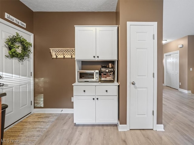 kitchen with a textured ceiling, light wood-type flooring, and white cabinetry